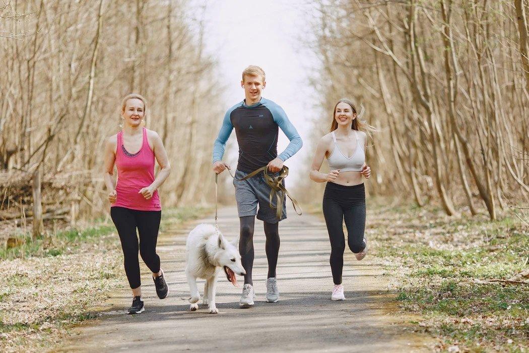three people running with a dog